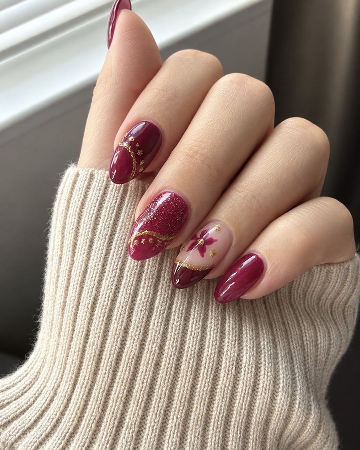 Almond-shape burgundy nails with gold line art and a hand-painted flower accent