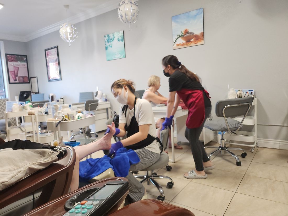 Inside the salon: two technicians at work beside pedicure chairs, with framed calming artwork on pale walls